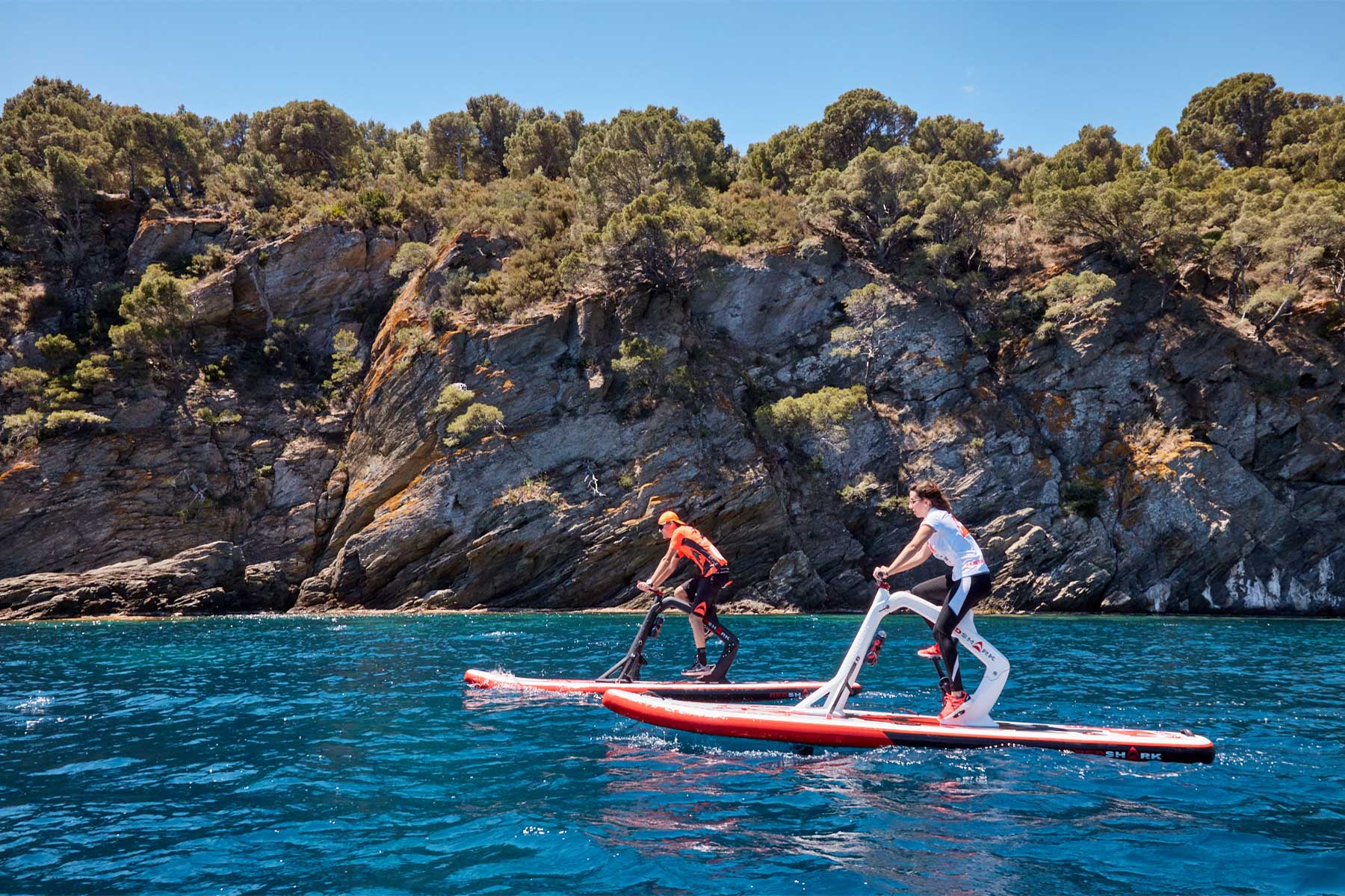 Un waterbike enjoy et un waterbike fitness sur l'eau montrant un sportif sur le waterbike fitness et une femme sur le waterbike enjoy qui profitent d'une expérience complète et unique de loisirs aquatiques.